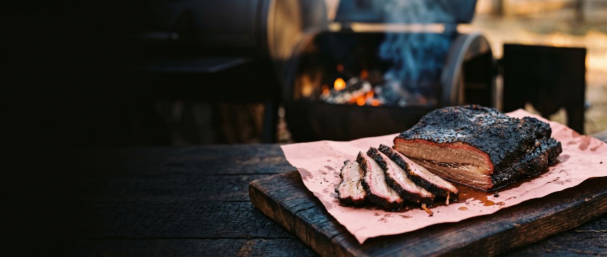 Sliced smoked brisket on butcher paper in front of an offset smoker