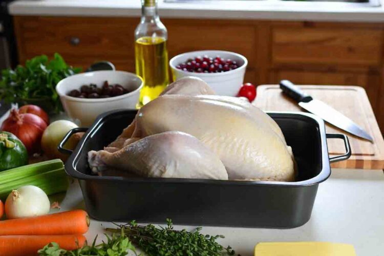 Thanksgiving prep checklist one week out: thawed turkey in roasting pan surrounded by fresh herbs, carrots, onions, celery, butter, and cranberry sauce on a rustic homestead kitchen counter